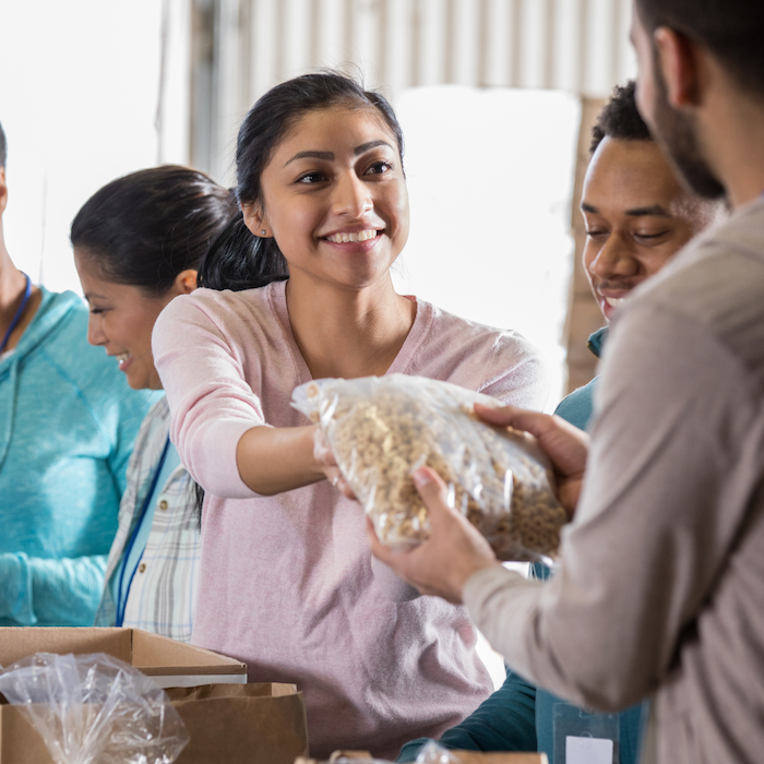 Volunteers at a food bank handing a bag of food to a recipient